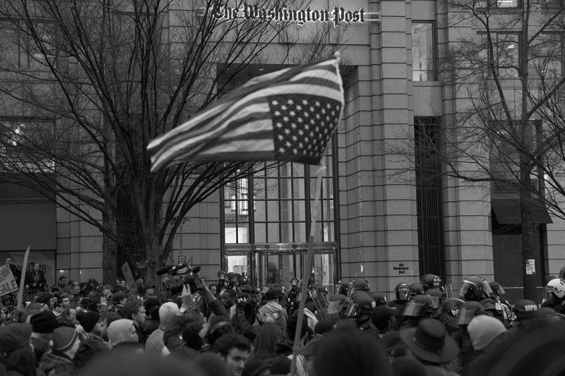 Manifestanții arborează un steag răsturnat ca semnal de alertă în fața birourilor The Washington Post din Washington D.C. în Ziua Inaugurării [ceremonia de învestire a președintelui Donald Trump], 20 ianuarie 2017. Foto: Ivan Sigal.