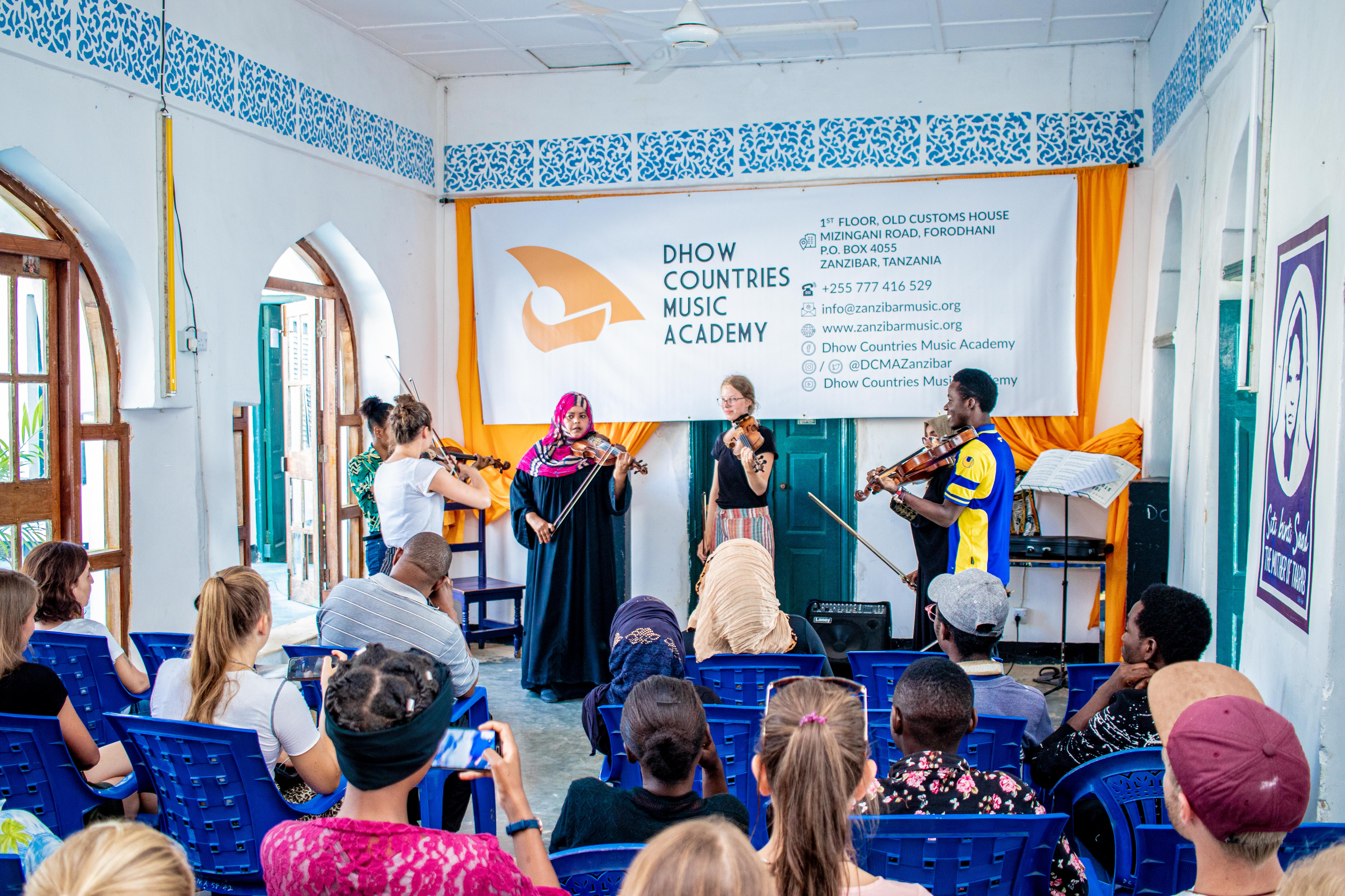Un groupe de violonistes se produit à l'académie de musique de Zanzibar dans une salle aux tons bleu et blanc.