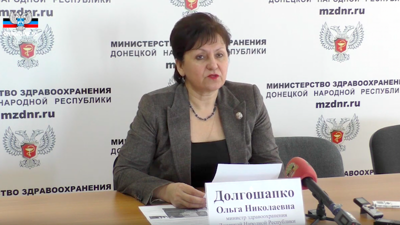 Olga Dolgochapko lit un communiqué devant un fond orné du logo du ministère de la Santé de la DNR