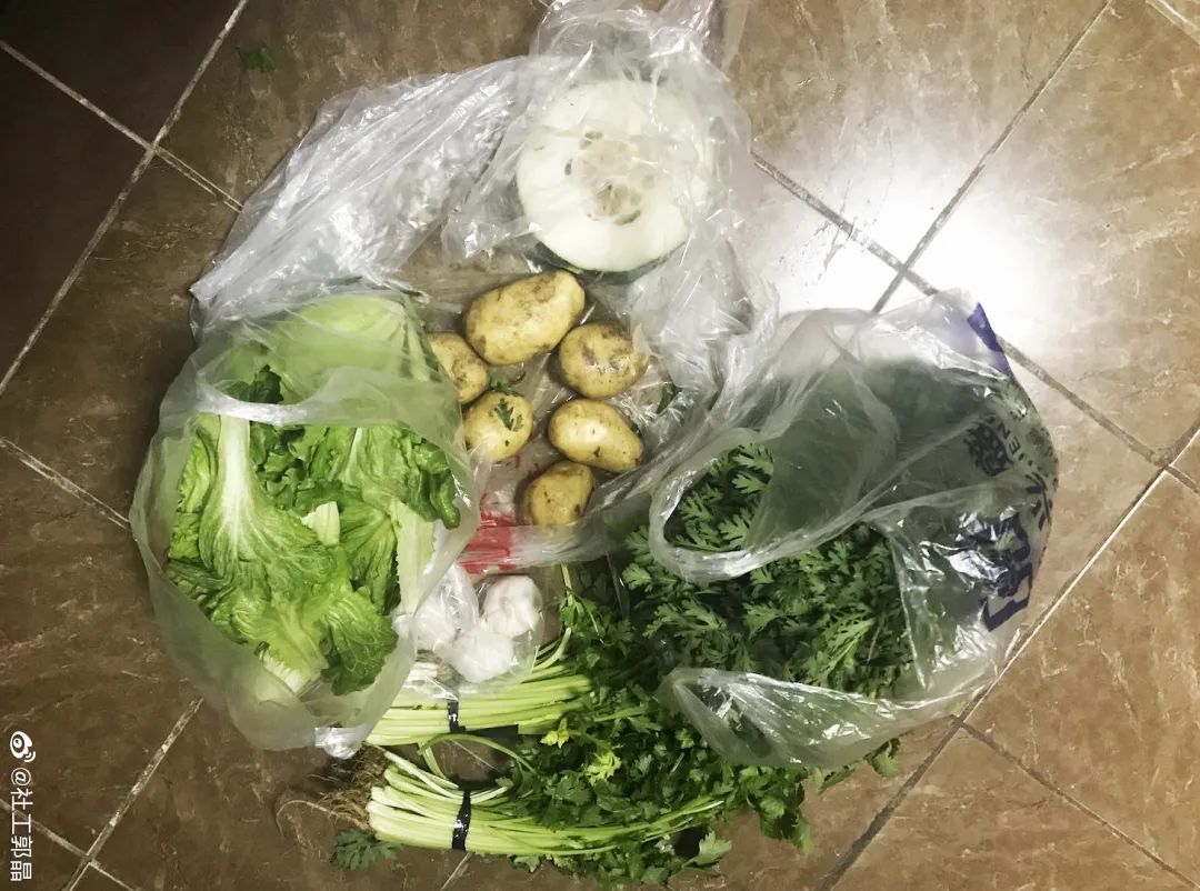 Un sac en platique posé sur le sol, rempli de légumes : pommes de terre, laitue, persil, concombre.
