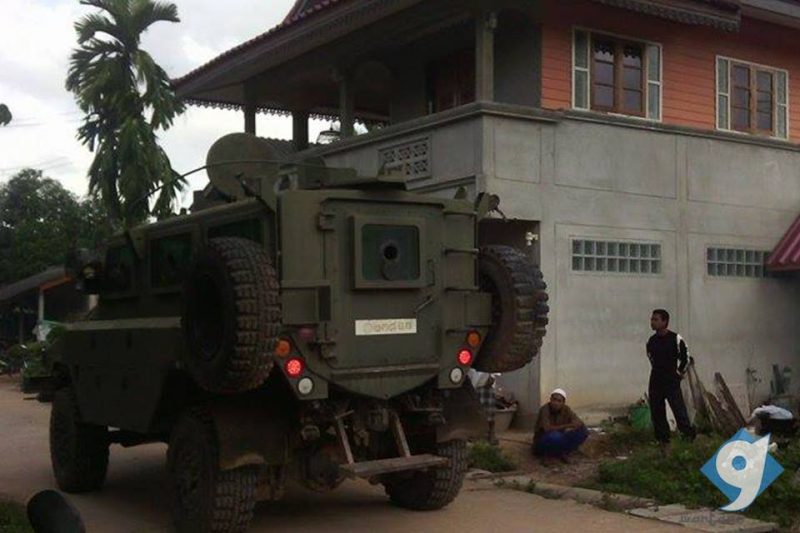 Un char militaire passe devant une maison à Pattani, tandis que deux habitants contemplent la scène.