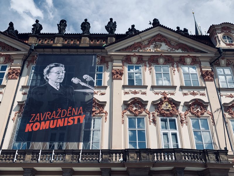 Grande affiche accrochée sur la façade d'un bâtiment, représentant Milada Horáková à son procès en noir et blanc, et portant le slogan « Zavražděna komunisty » en rouge (Assassinée par des communistes).