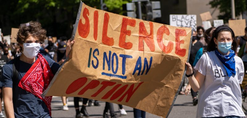Deux jeunes manifestants blancs portant des masques tiennent une pancarte "Le silence n'est pas de mise" pendant une marche Black Lives Matter.