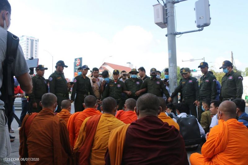 Un groupe de moines en robe safran assis par terre fait face à un groupe de policiers qui bloquent leur passage.