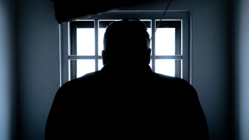 Un homme de dos. Son image est dans le noir dans un souci d'anonymat. Il se trouve dans une pièce assez petite. L'homme est plutôt de stature imposante. Il fait face à une fenêtre.