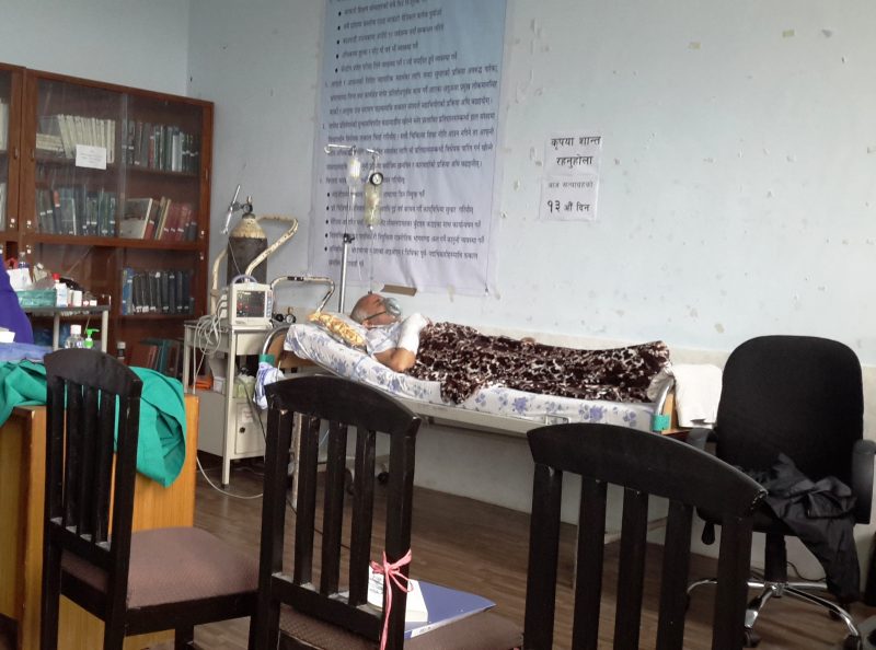 Le médecin népalais en grève de la faim est allongé sur un lit, le bras bandé et le visage connecté à un respirateur qui semble vétuste.