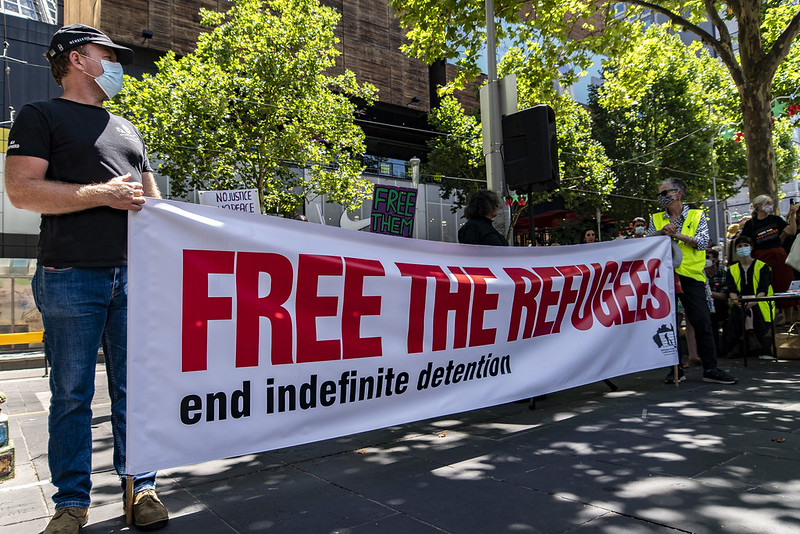 Des personnes manifestent dans la rue. Ils tiennent une banderole sur laquelle est écrit "Libérez les réfugiés, mettez fin à la détention indéfinie". 