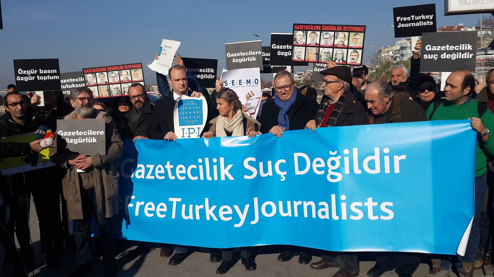 On peut voir un groupe de personnes tenant des banderoles et des pancartes avec écrit en turc et en anglais Free Turkey Journalists