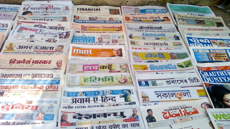 Indian Newspapers for sale at a vendors shop in New Delhi. Image via wikipedia by Shajankumar. CC BY-SA 3.0.