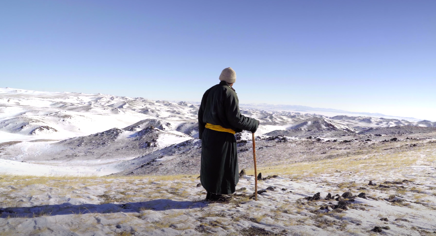 Un éleveur mongol regarde par-delà les montagnes enneigées.